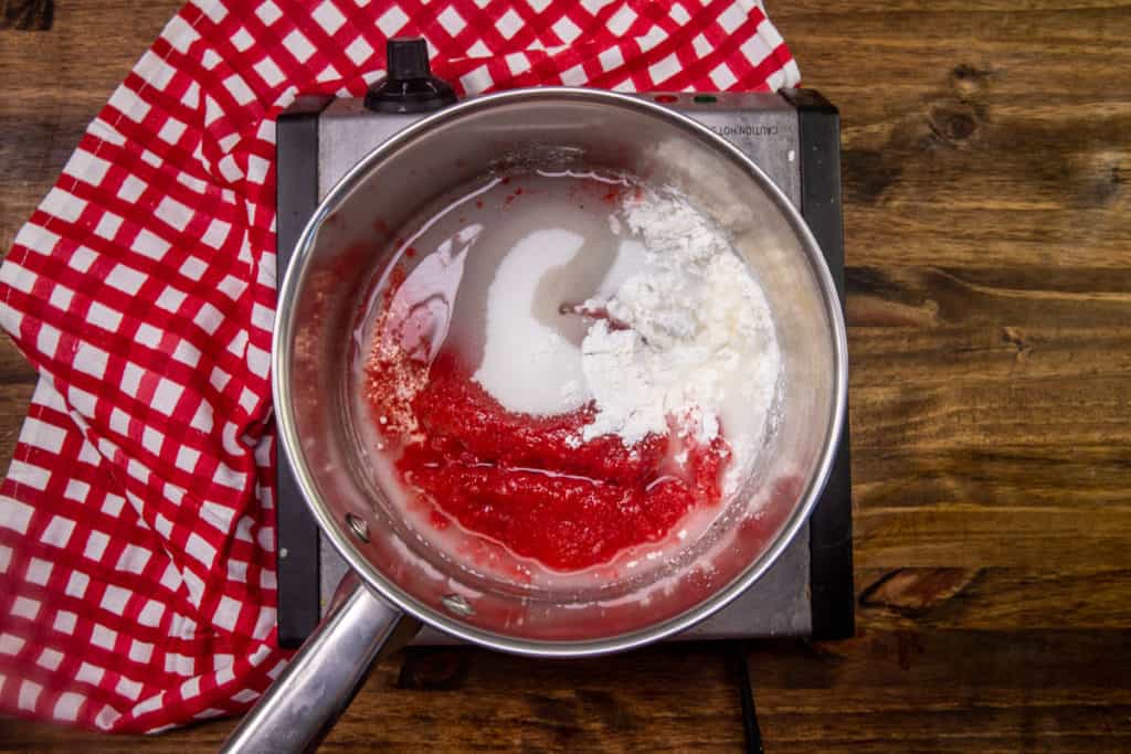 crushed strawberries, corn starch and water added to a silver sauce pan on an electric countertop burner.