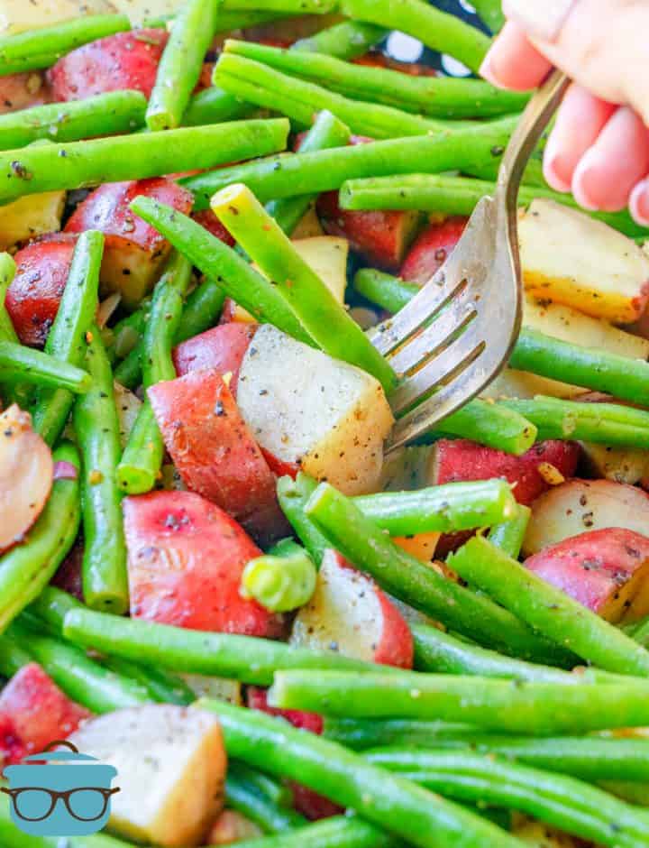 closeup photo of a fork piercing into a grilled diced potato with green beans.