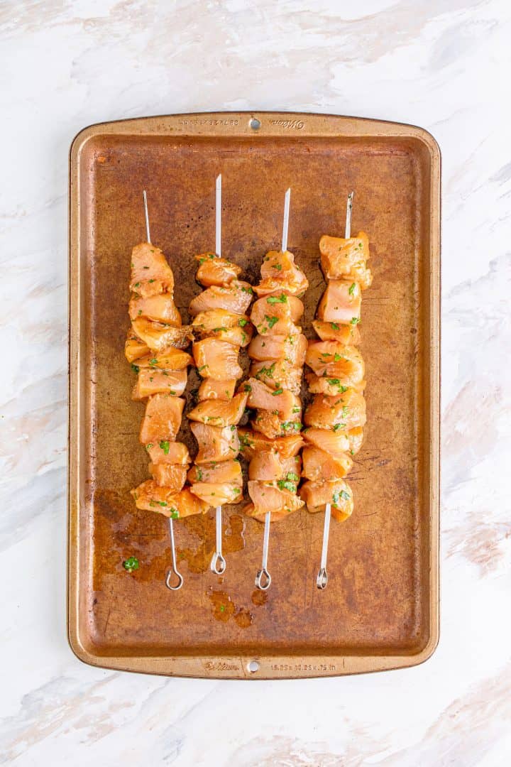 marinated chicken pieces threaded on metal skewers and placed on a baking sheet. 
