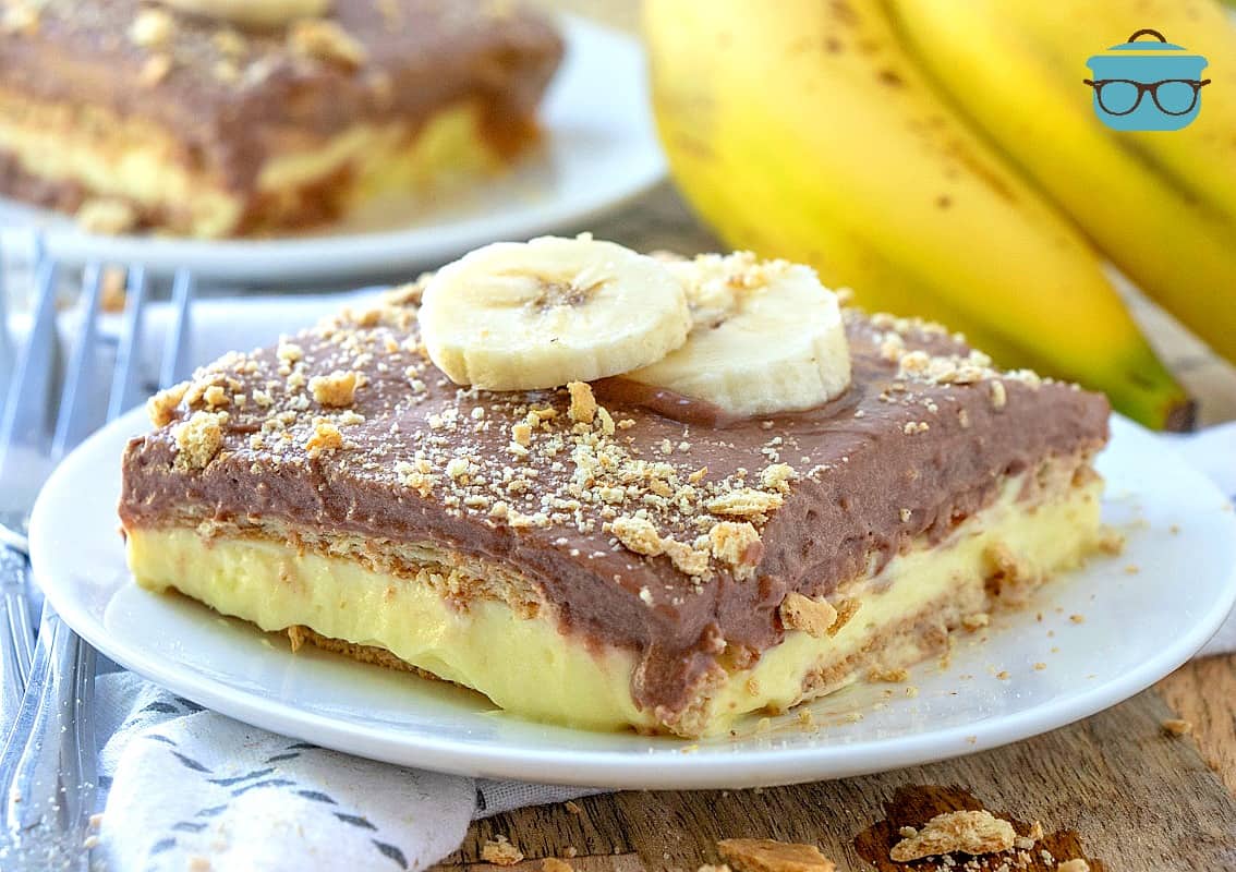 a slice of chunky monkey cake on a small round white plate and topped with two sliced of bananas.