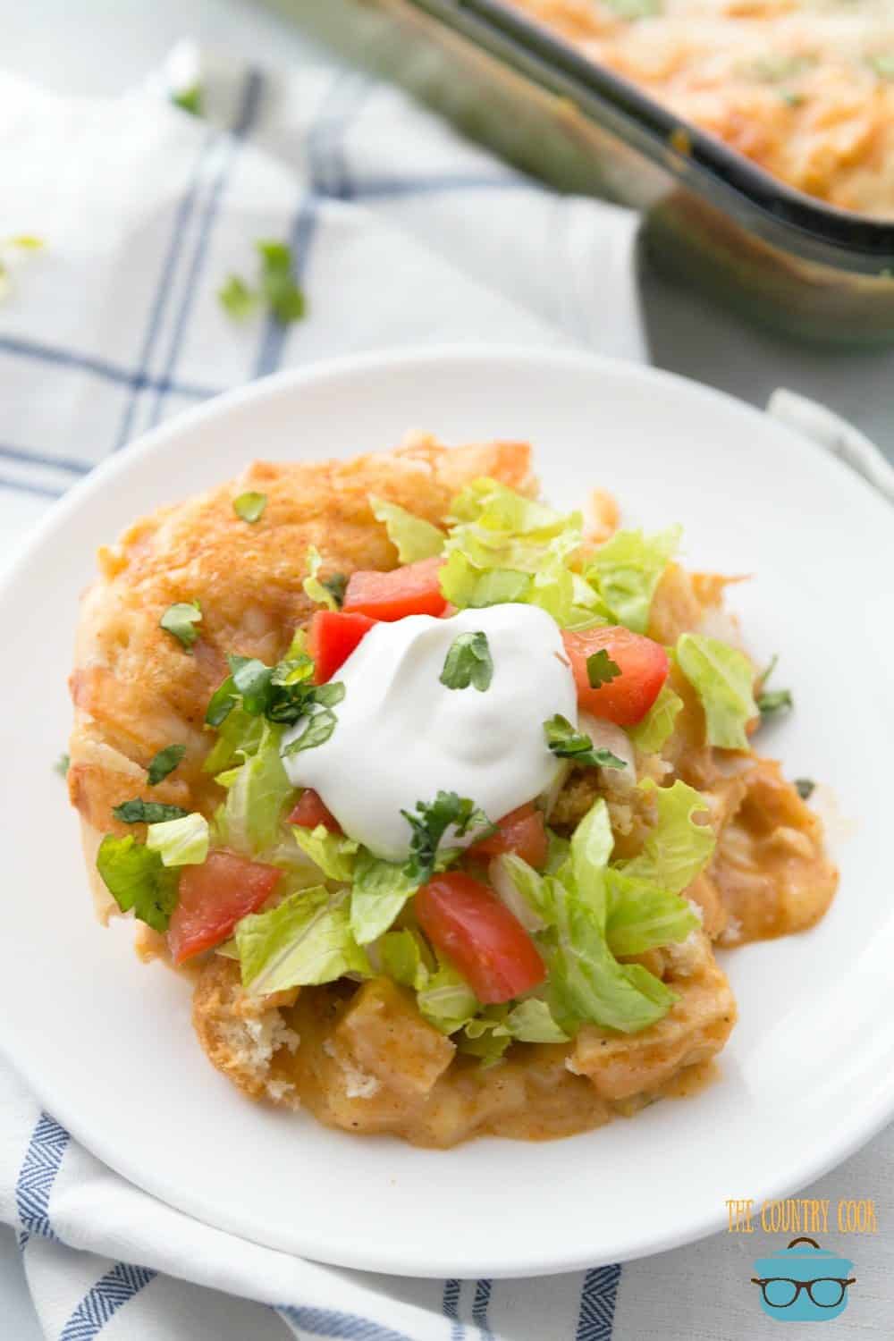 Chicken Enchilada Bake on a plate served with sour cream, lettuce and diced tomatoes.