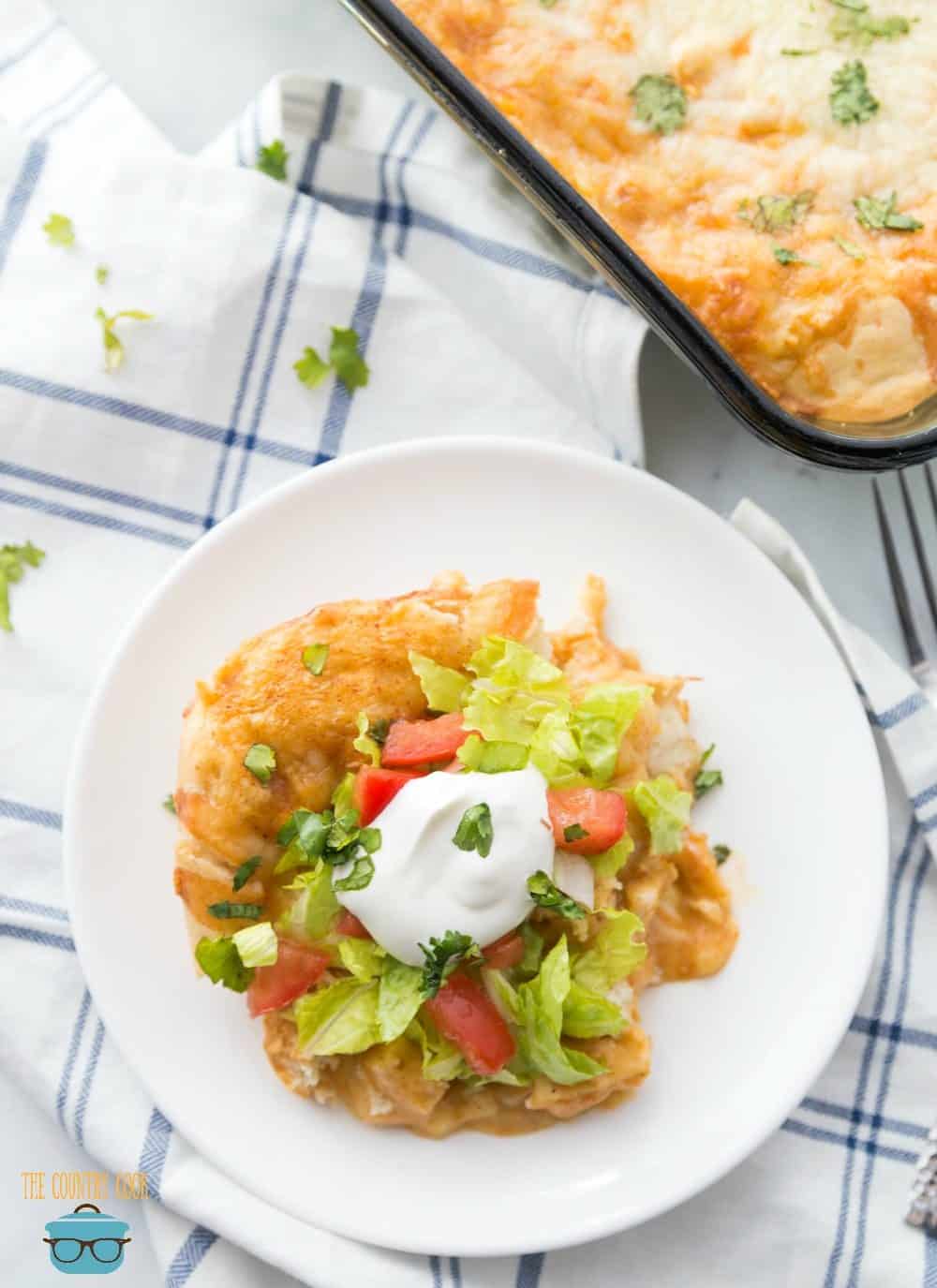chicken enchilada casserole shown topped with lettuce, tomato and sour cream on a small round white plate.