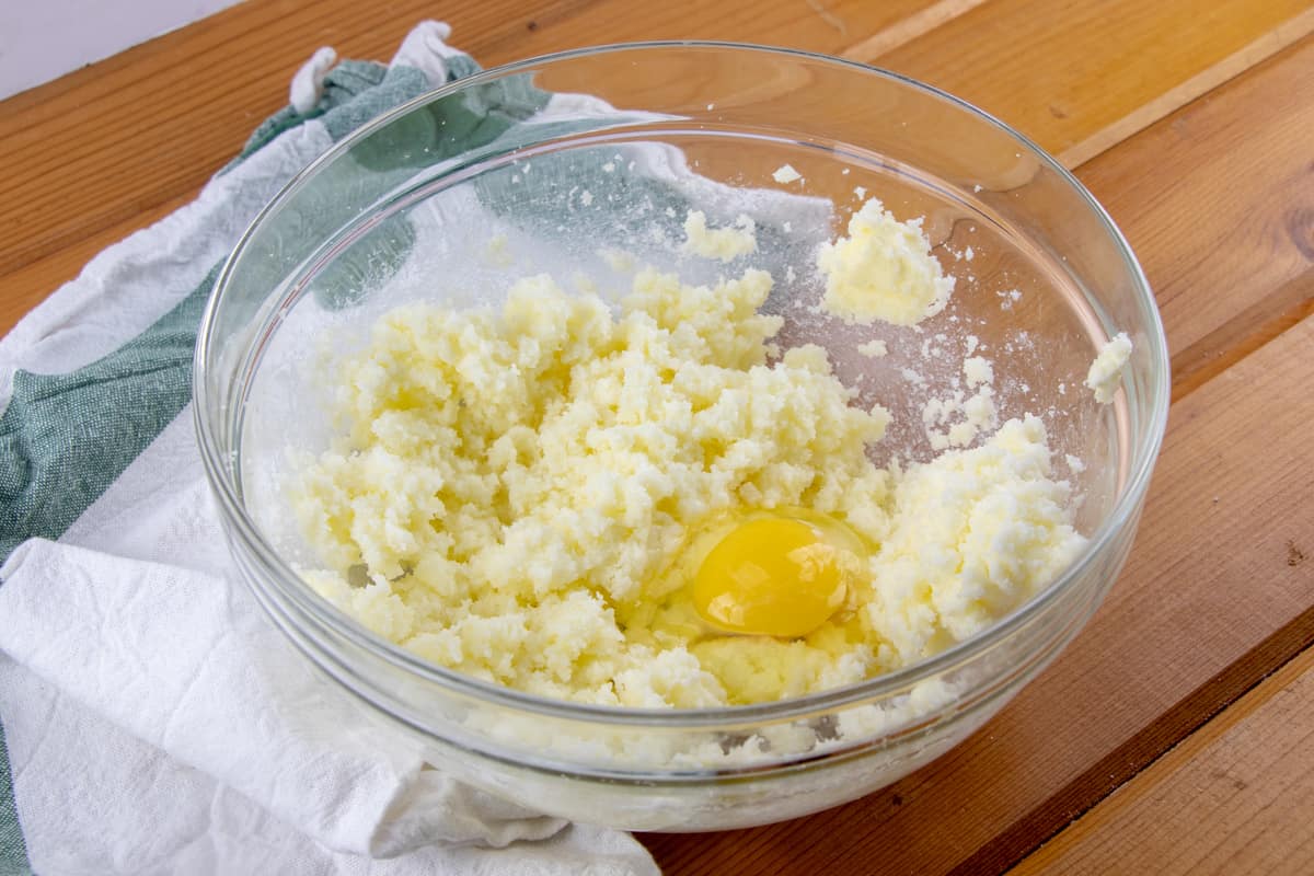 adding eggs to butter and sugar mixture in a glass bowl.