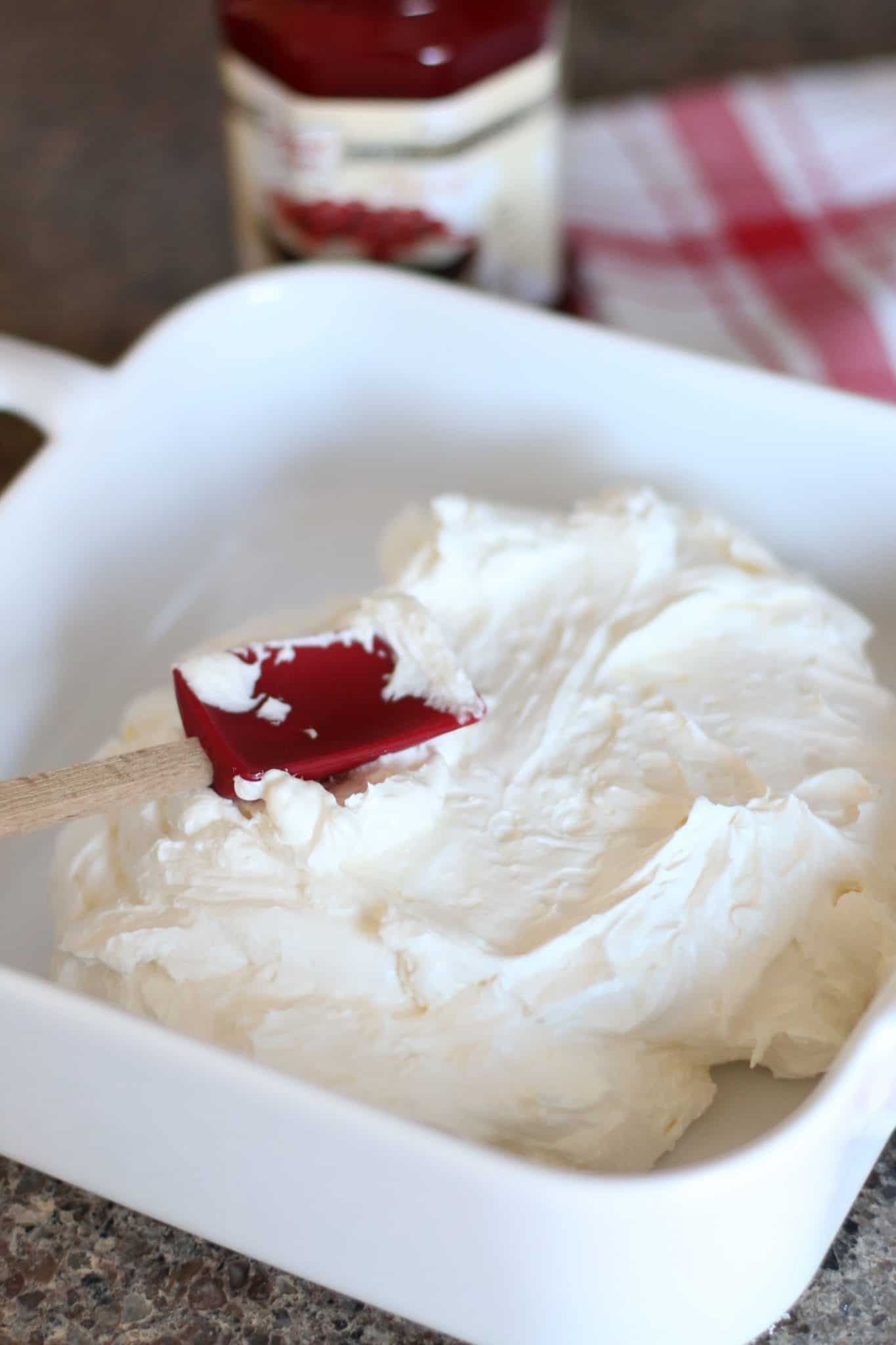a small red spatula smoothing the cream cheese mixture into a white baking dish.