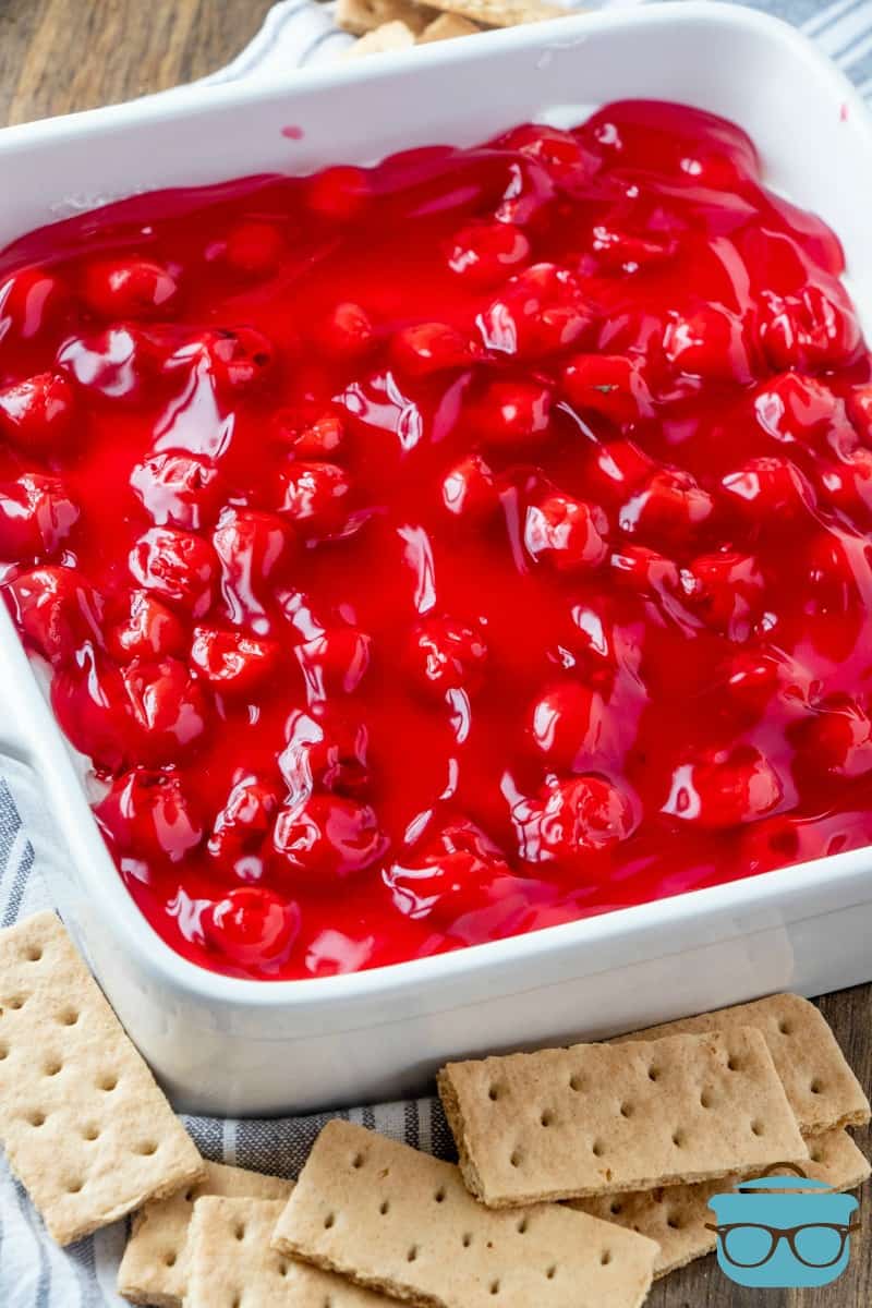 cherry cheesecake dip shown in a white square baking dish with graham crackers spread around the outside.