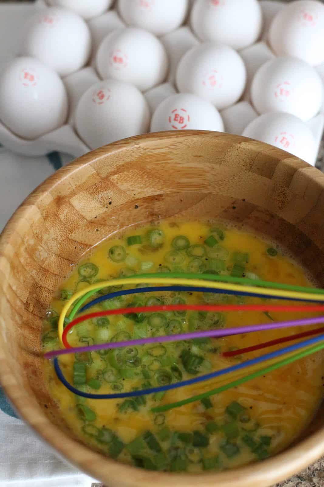 sliced green onions whisked together with eggs in a bowl.