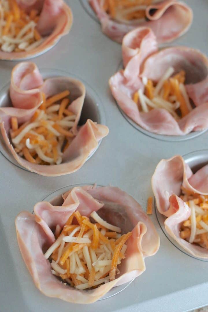 shredded cheese added into ham cups in muffin tin.