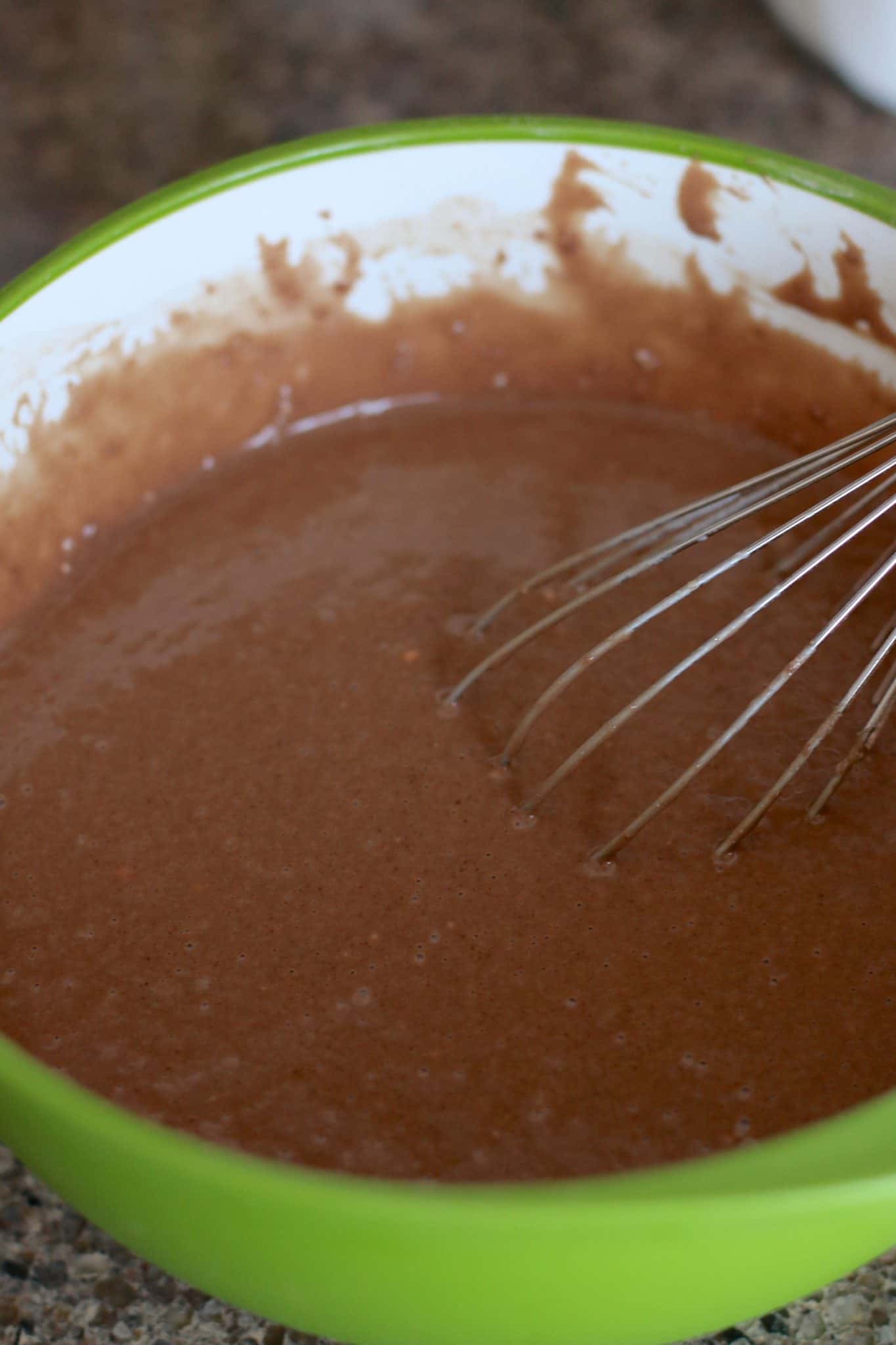 whisking chocolate cake batter in a bowl.