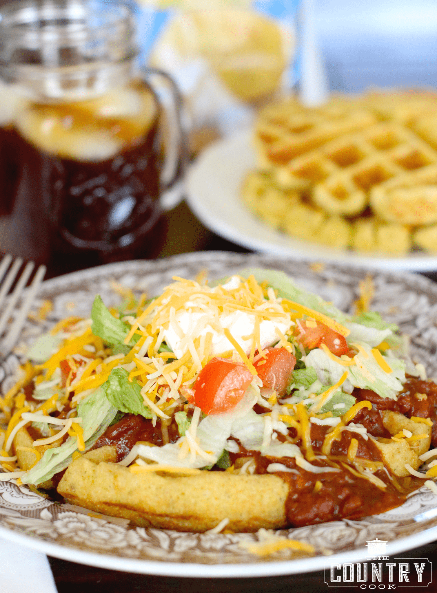 Cornbread Waffles with Chili and Fixins shown on a brown and white plate with a fork on the side. 