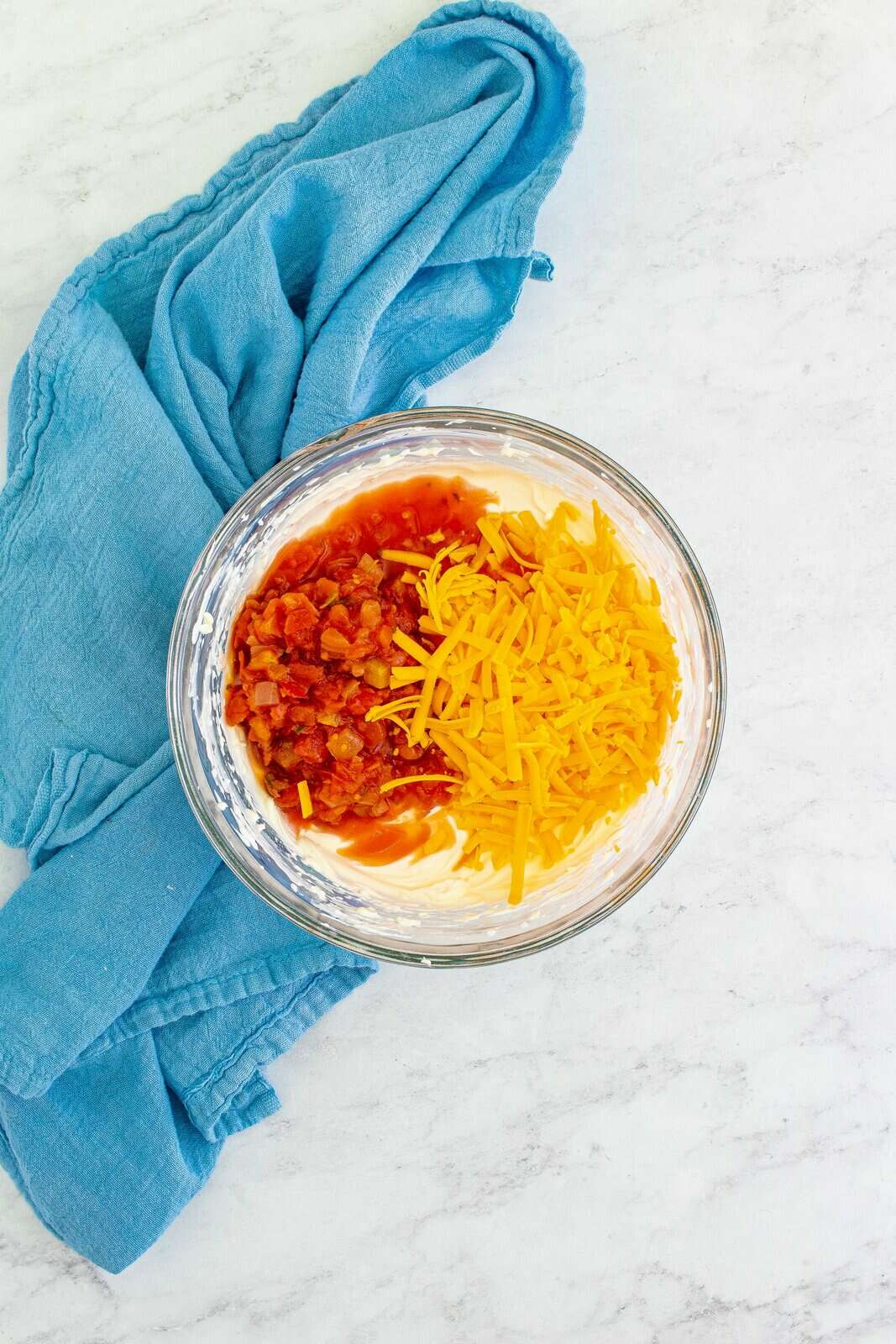 salsa and cheddar cheese added to cream cheese and sour cream mixture in a clear bowl. 