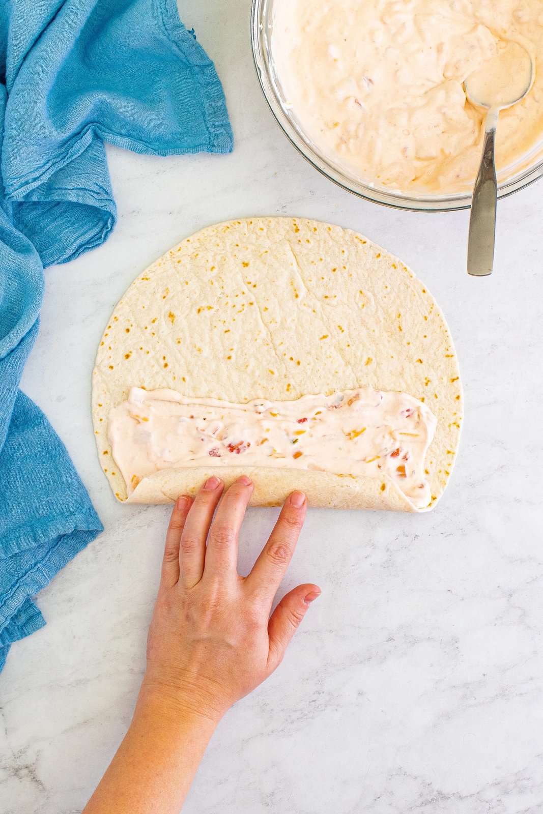 a hand showing rolling up a cream cheese filled tortilla. 
