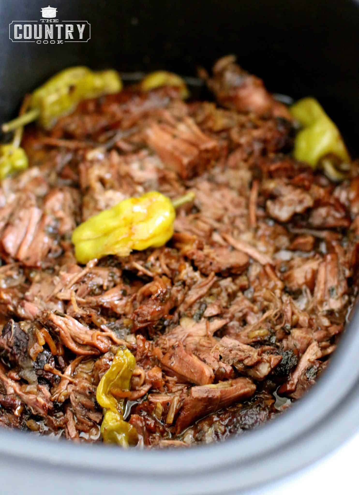 fully cooked and shredded Mississippi pot roast in a slow cooker with peperoncini peppers on top.