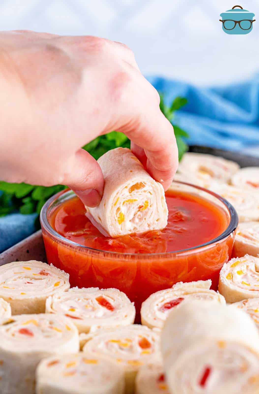a hand dipping a pinwheel into a bowl of salsa. 