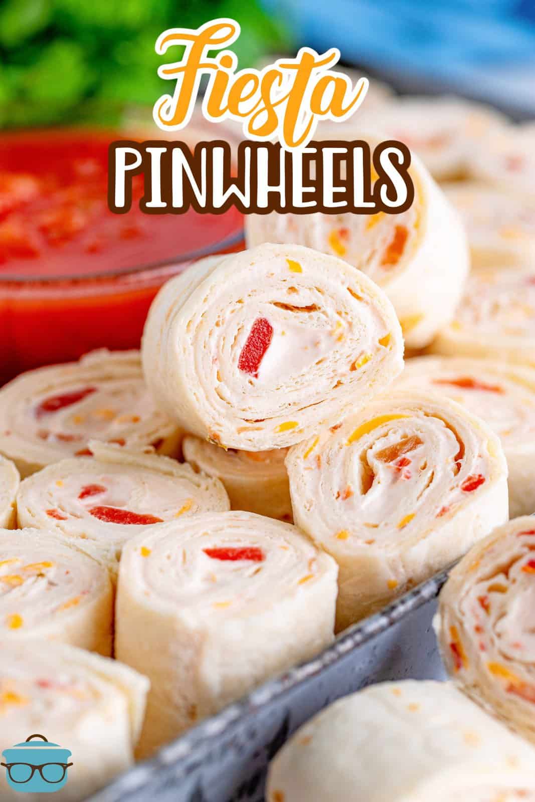 close up photo of stacked fiesta pinwheels on a metal tray with a bowl of salsa in the background. 