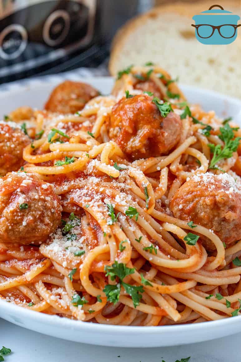 close up of Spaghetti and Meatballs in a white bowl with slices of bread in the background.
