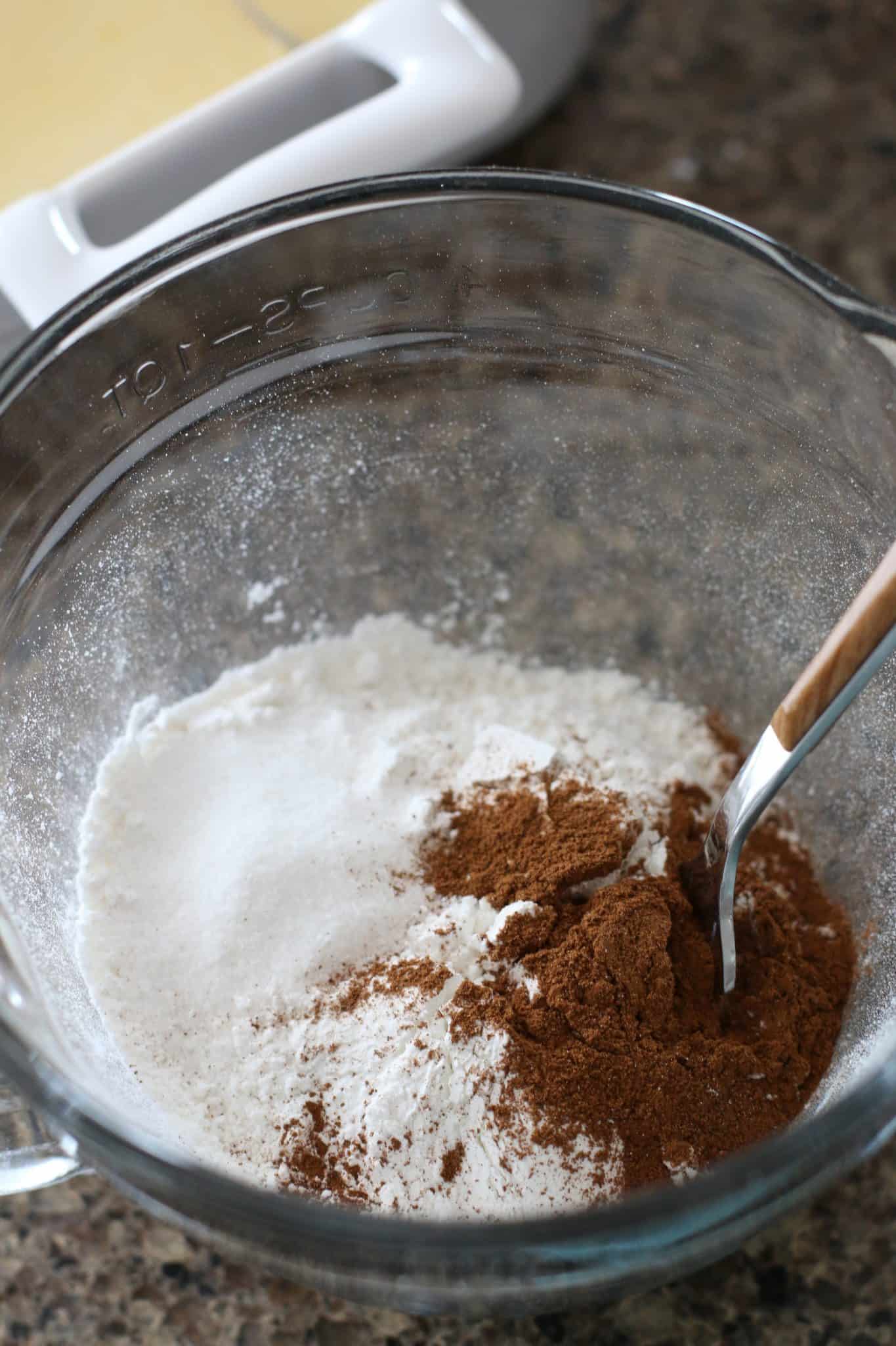 flour, cinnamon, baking powder being mixed together with a fork in a clear measuring cup.