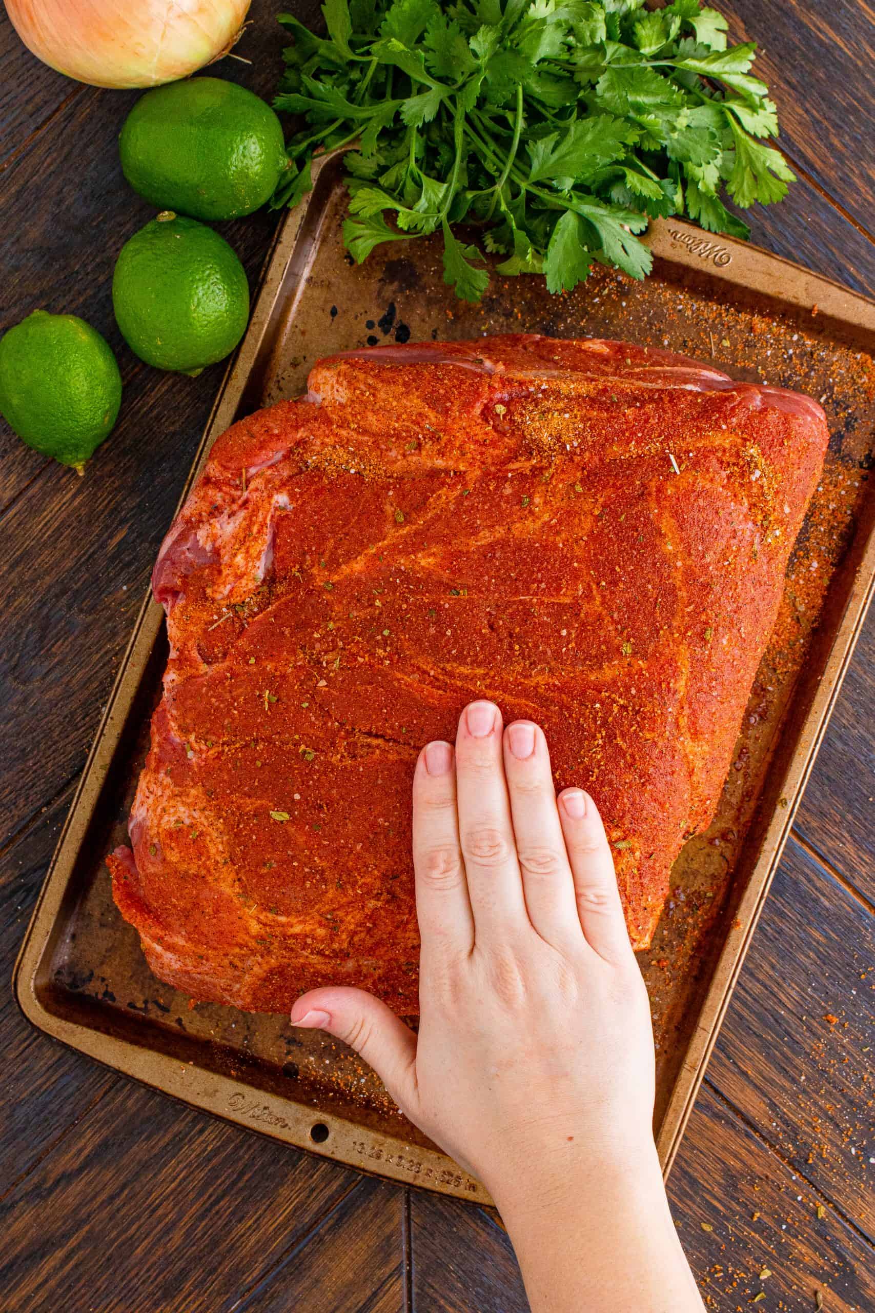 rubbing seasoning and spices into a pork roast on a baking tray.