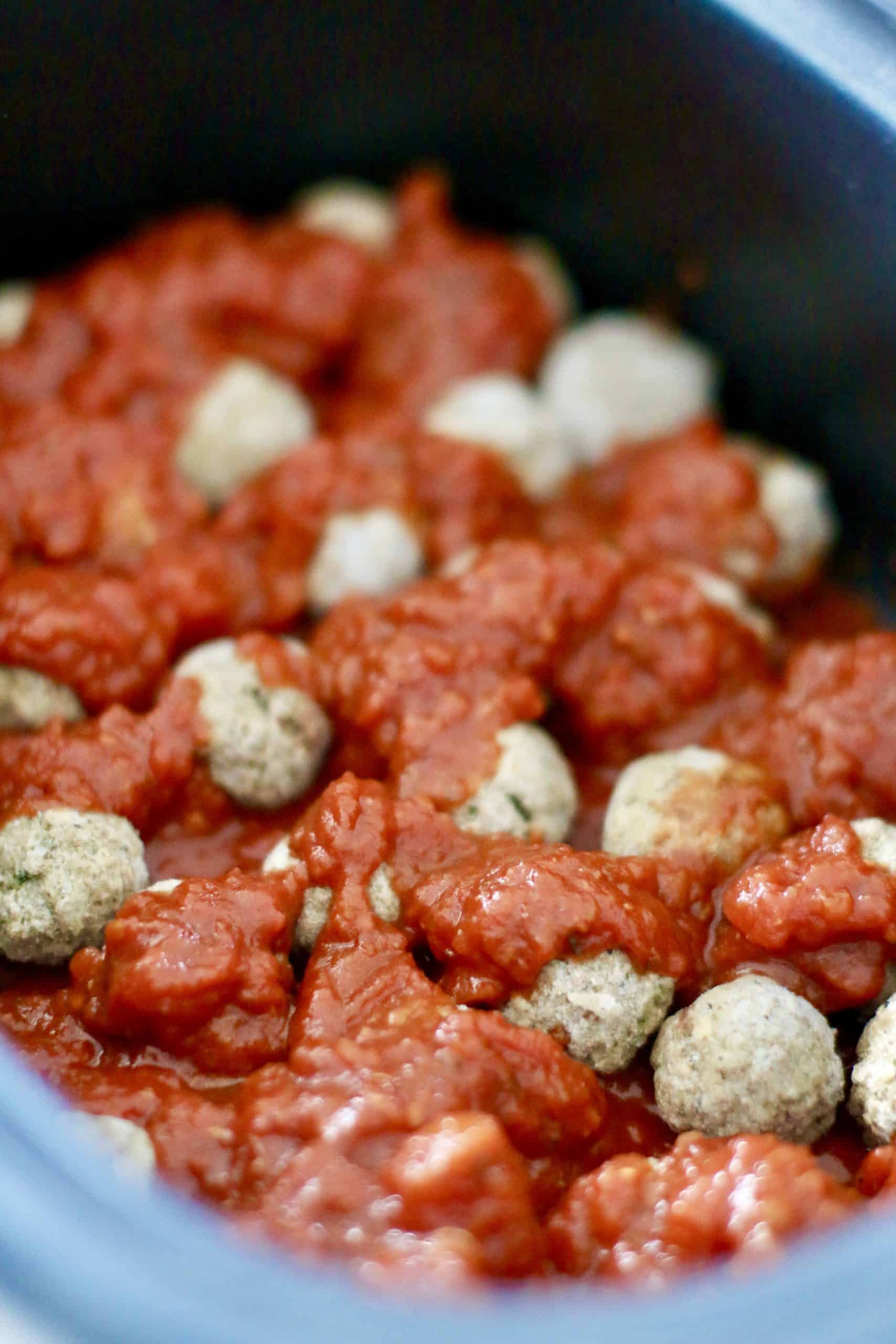 spaghetti sauce poured over frozen meatballs in an oval slow cooker.