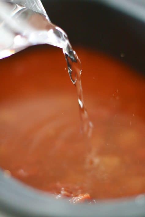water pouring into crock pot filled with spaghetti sauce