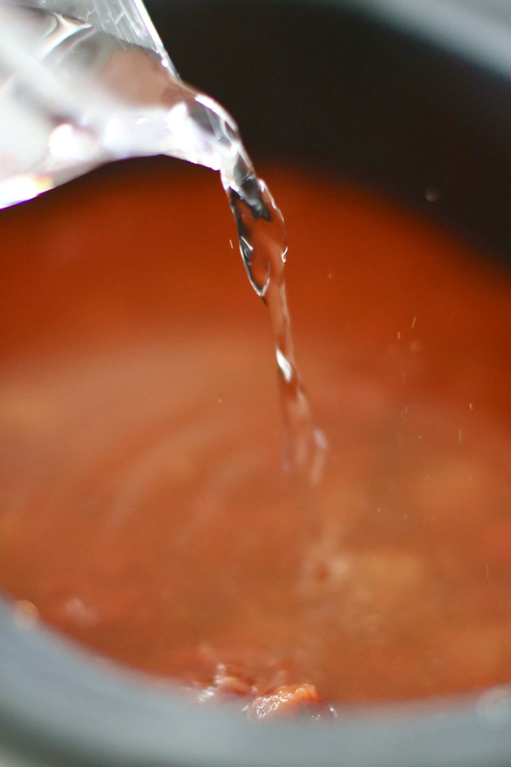 water pouring into crock pot filled with spaghetti sauce.