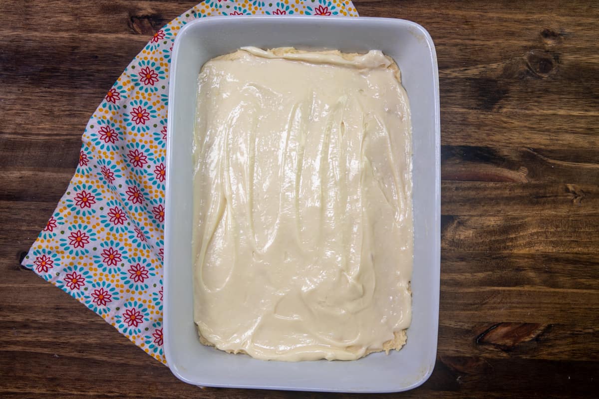cheesecake batter spread on top of cake batter in a large white baking pan.
