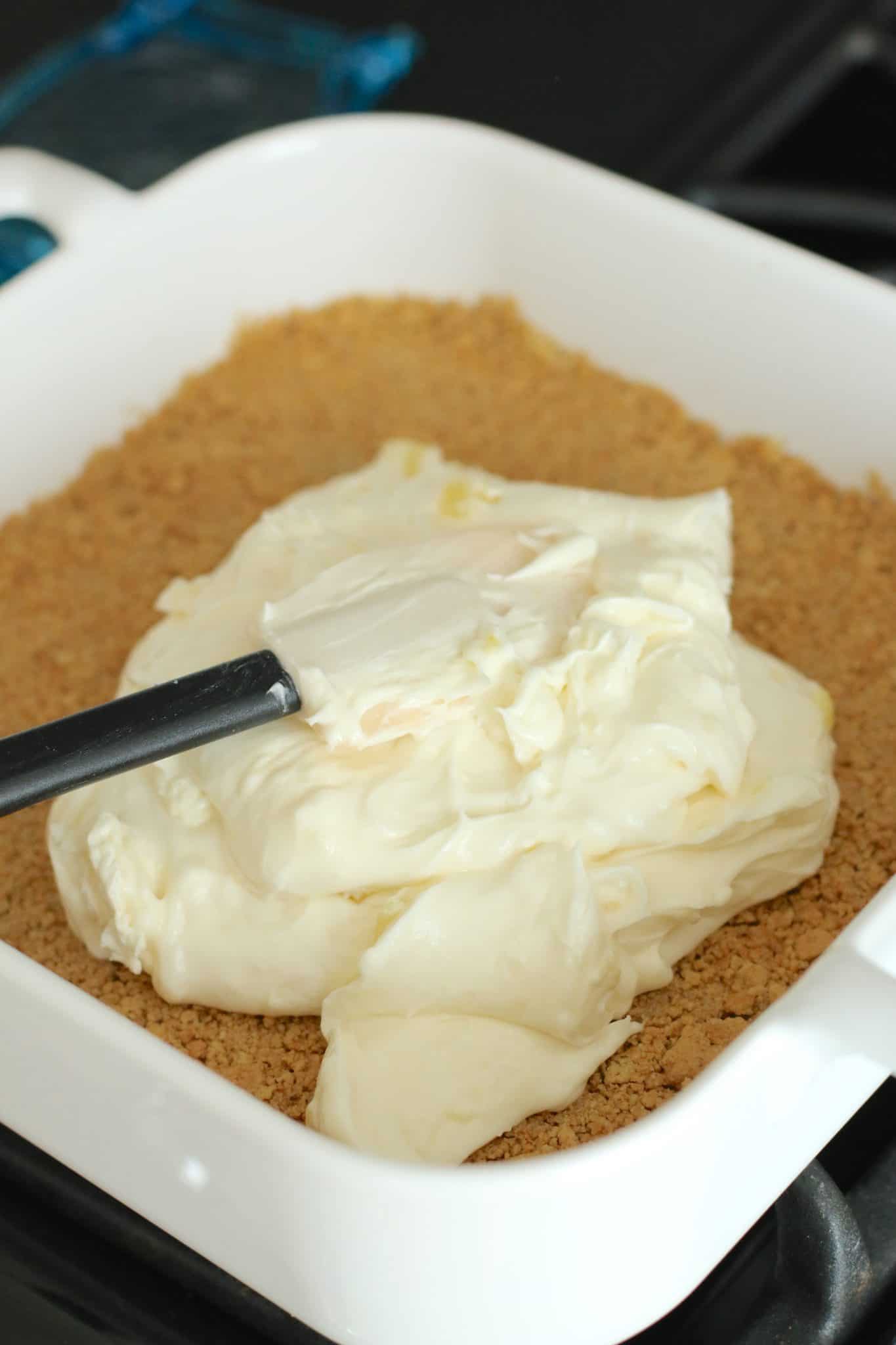 cream cheese mixture being spread on graham cracker crust