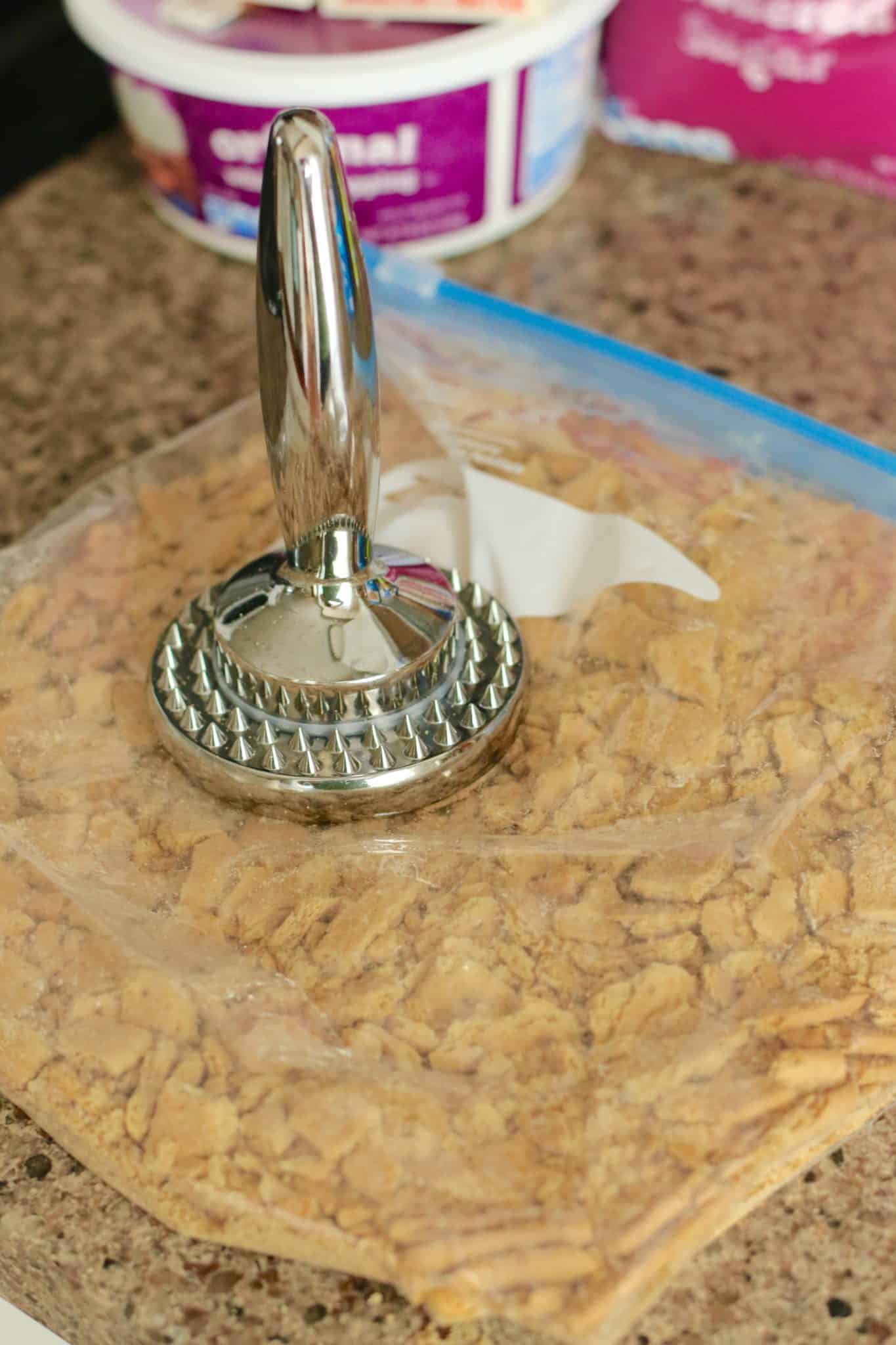 graham crackers in a zip top bag being crushed with a meat tenderizer