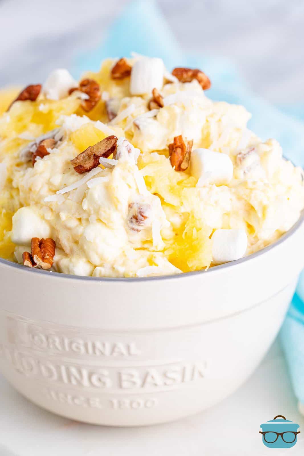 pineapple fluff, topped with chopped pecans in a white serving bowl on a white wood surface. 