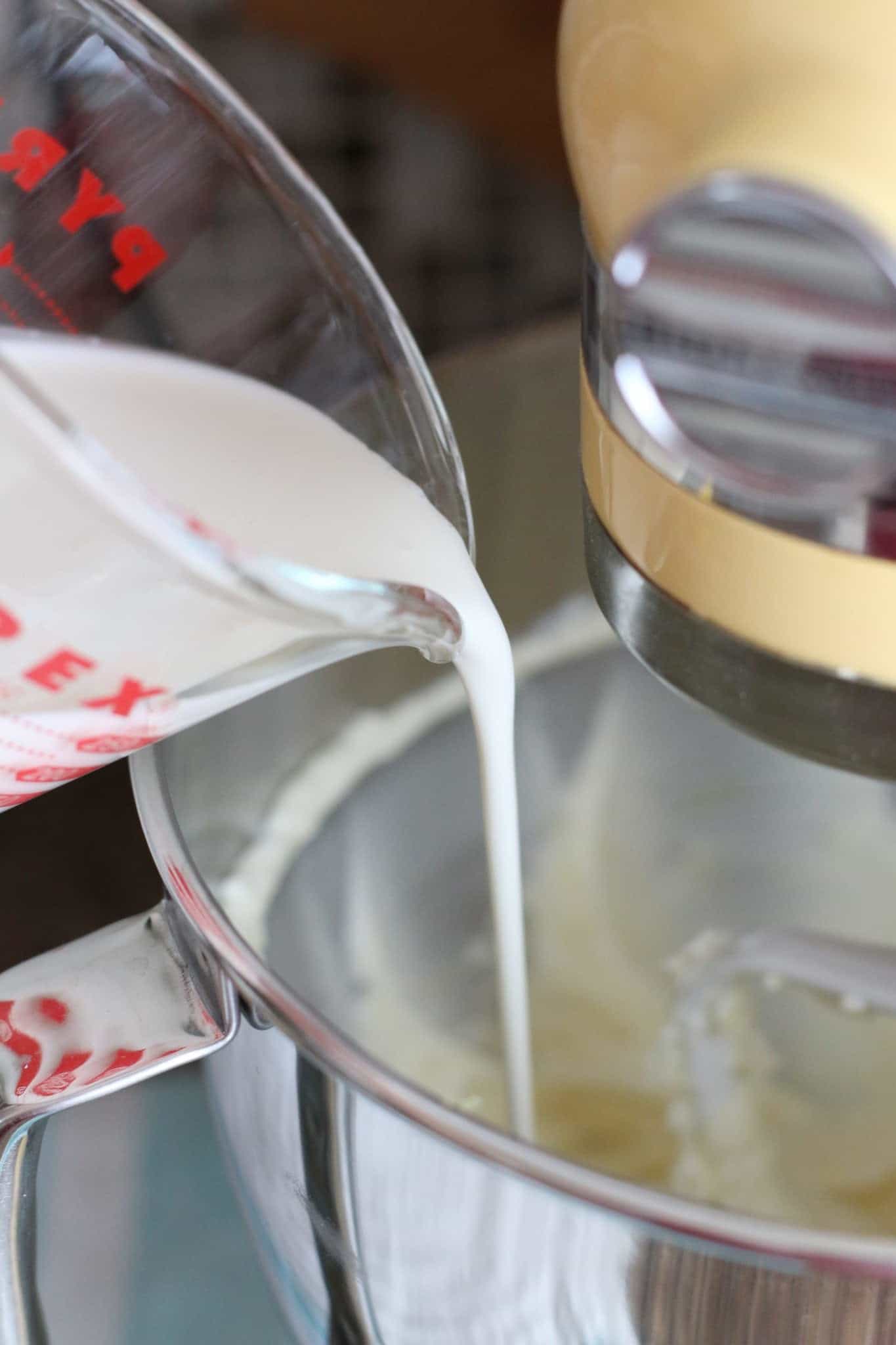 adding heavy cream to cream cheese and sugar mixture in KitchenAid stand mixer.