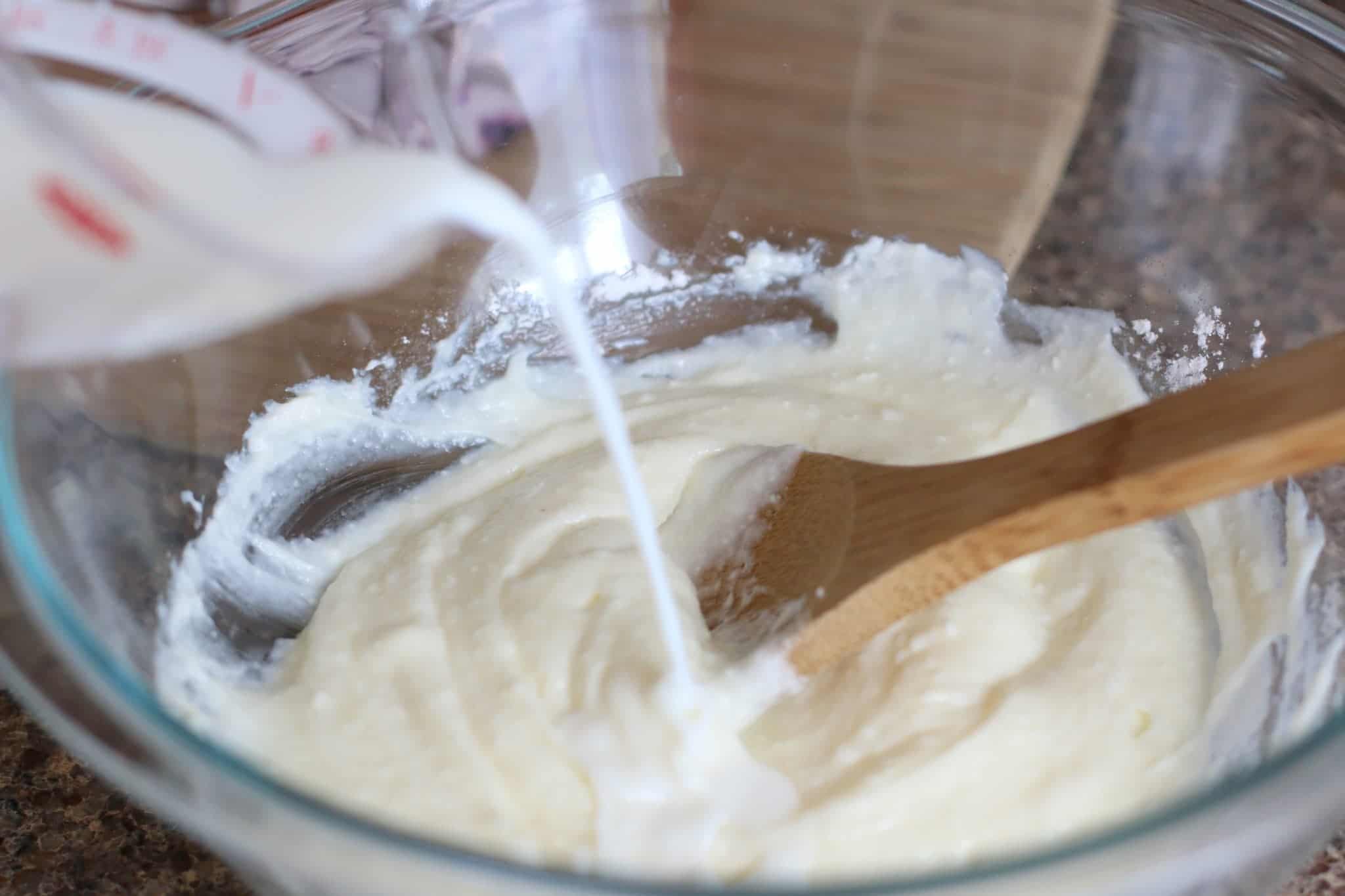 mil being poured into cream cheese mixture in a bowl.