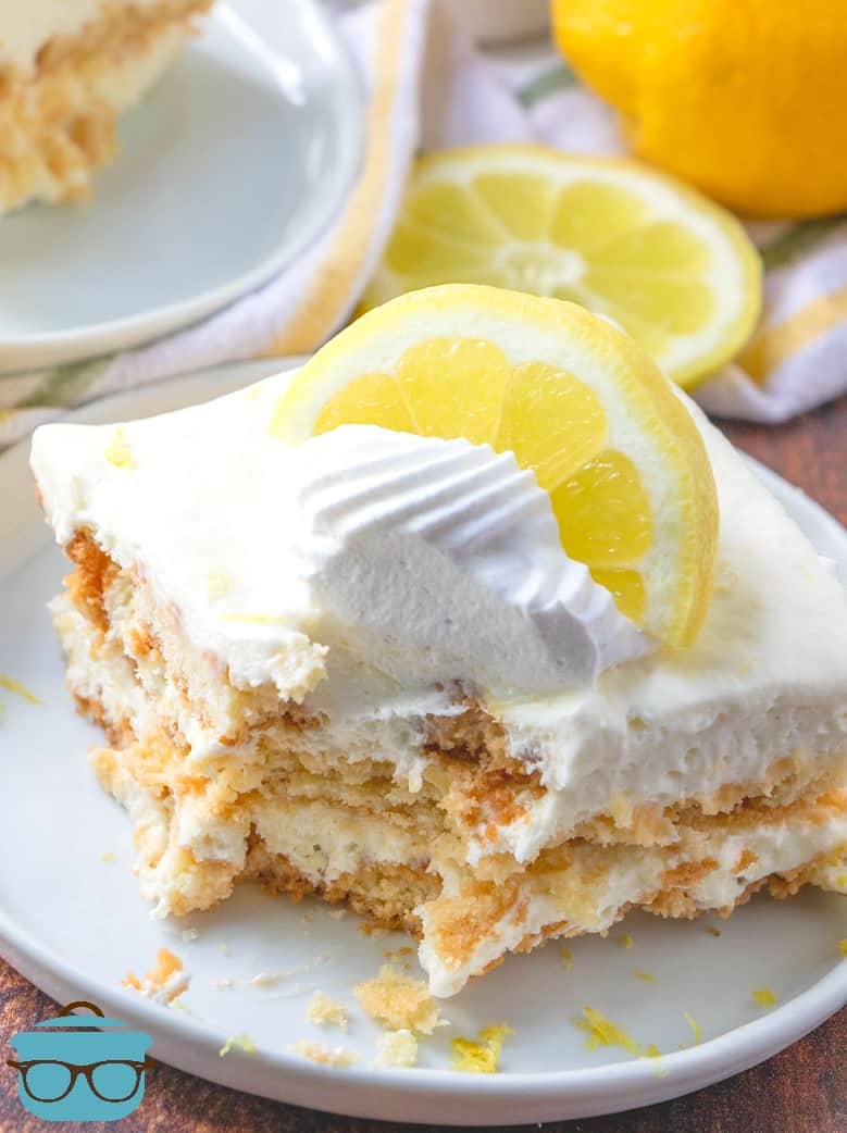 No-Bake Lemon Icebox Cake slice served on a white plate topped with a dollop of whipped cream and a lemon slice.