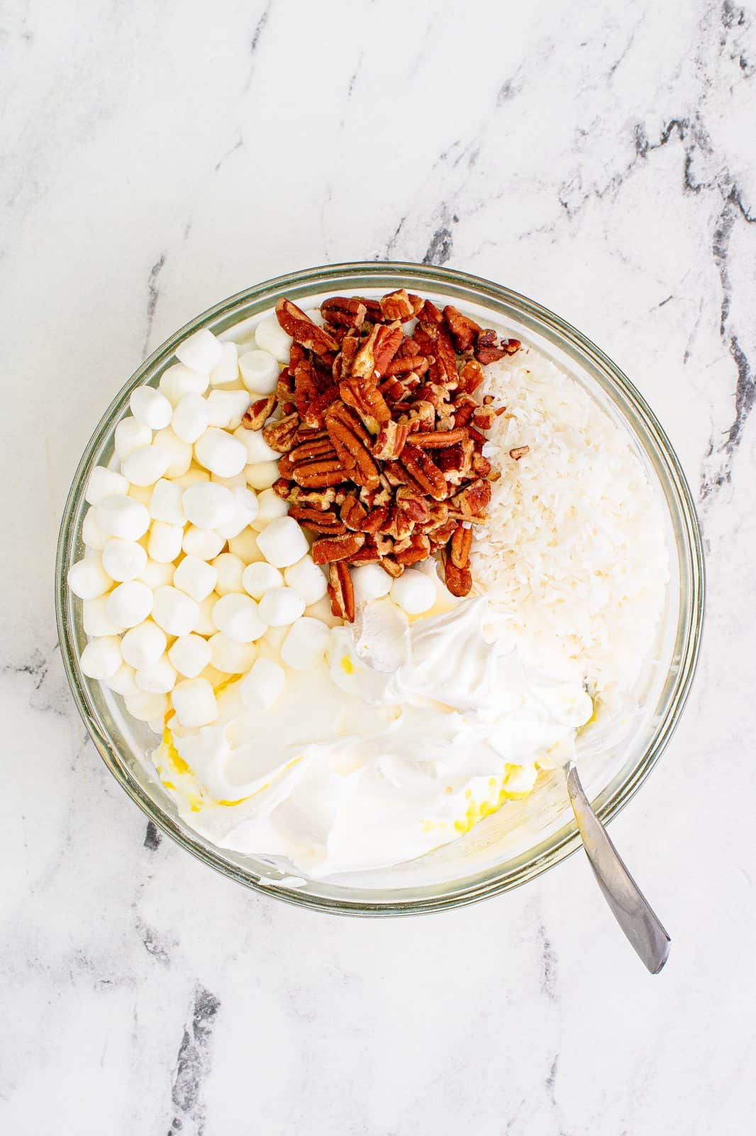 mini marshmallows, chopped pecans and Cool Whip added to pineapple in a clear bowl. 