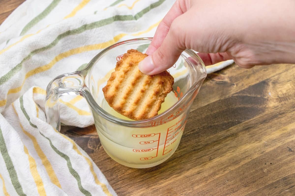 dipping a cookie into lemon juice in a measuring cup.