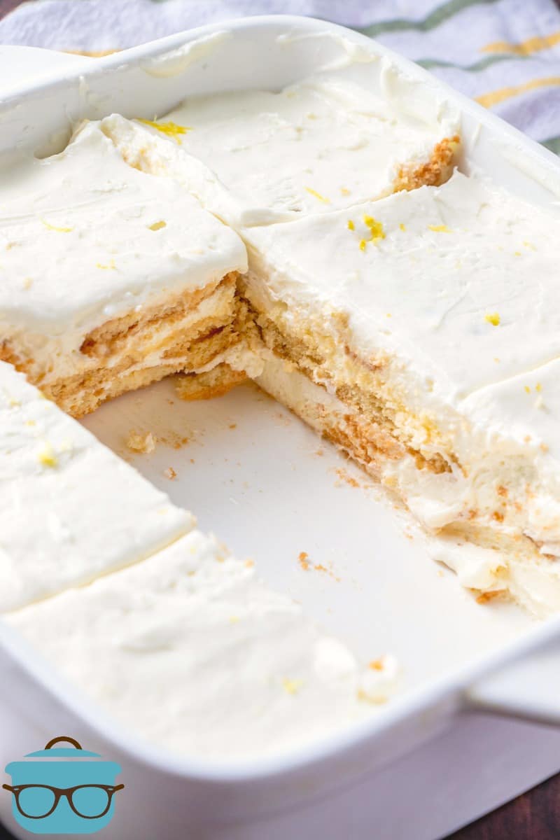 lemon icebox cake shown in a white serving dish, cut into slices with two slices missing.