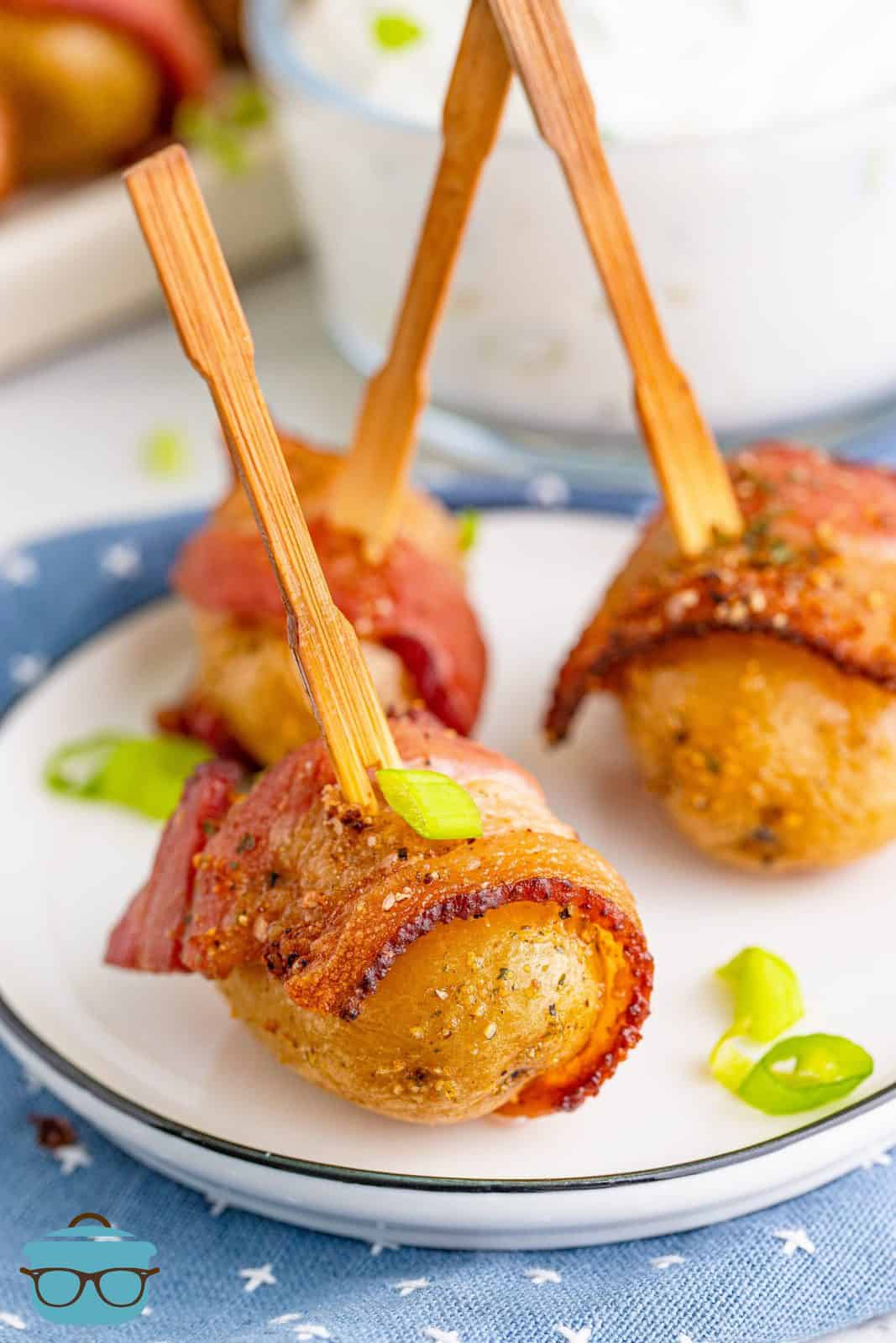 three bacon wrapped potatoes on a small white appetizer plate. 