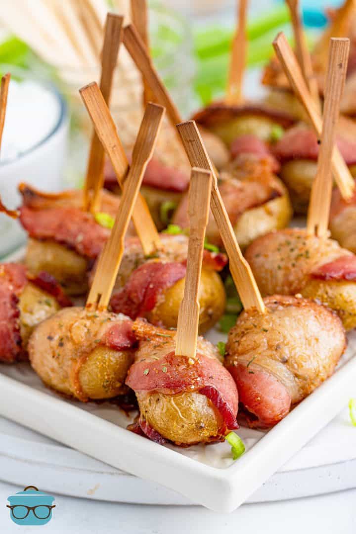a white tray with bacon wrapped potatoes that have toothpicks in them.