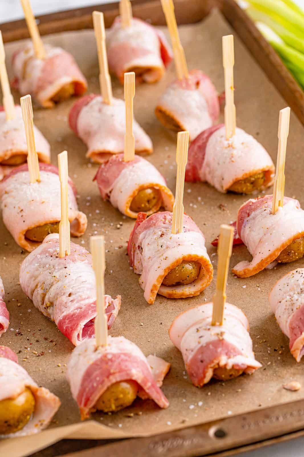 bacon wrapped baby potatoes secured with toothpicks on a parchment lined baking sheet.
