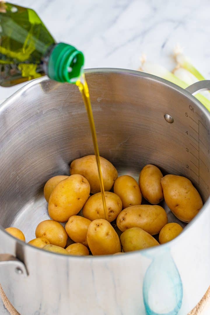 pouring olive oil over cooked baby potatoes in a pot.