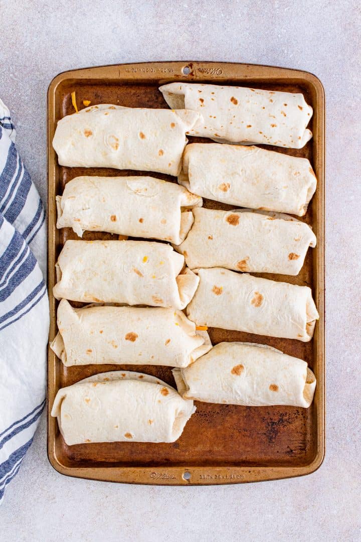 ten folded breakfast burritos on a baking tray.