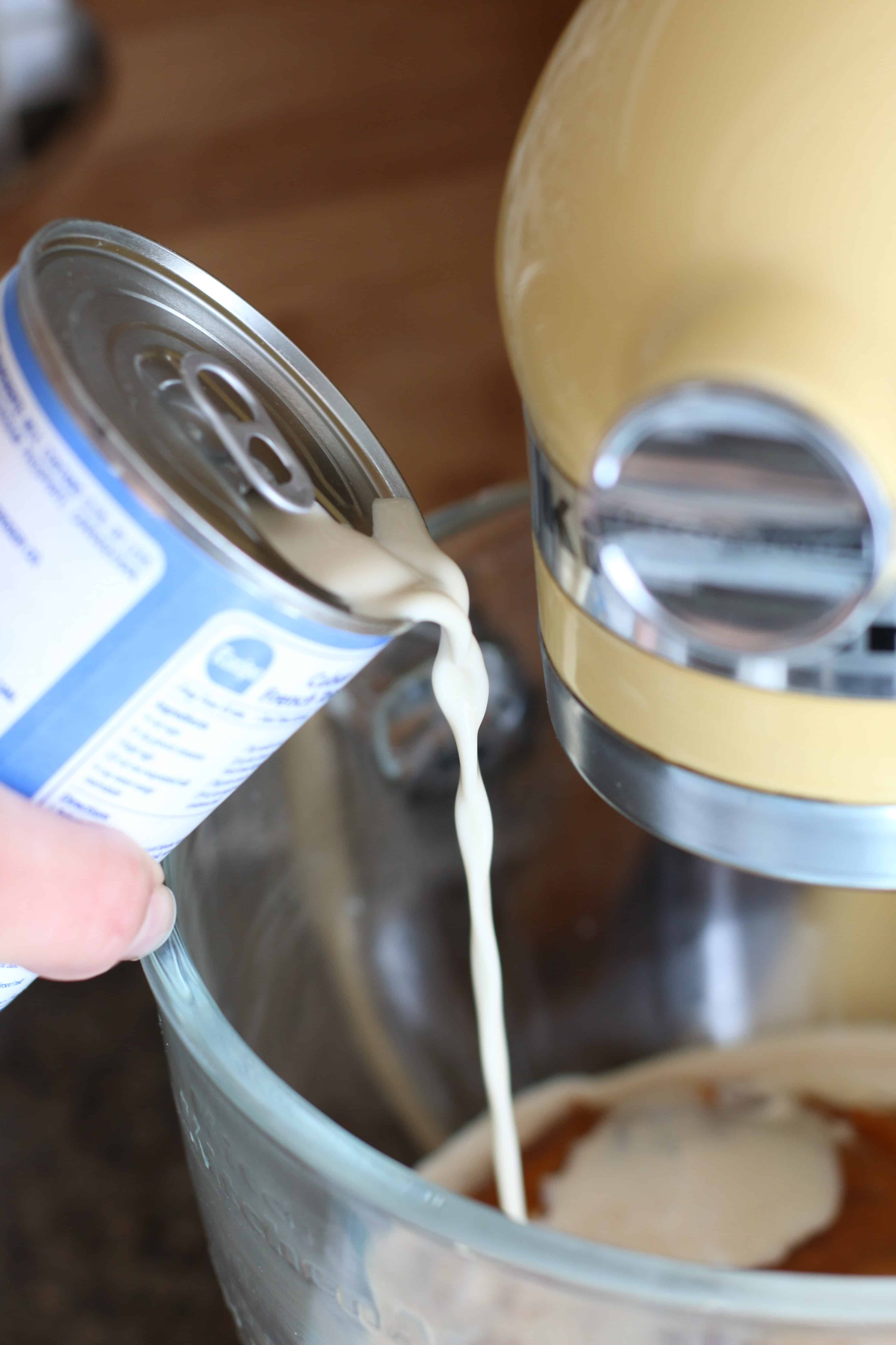 pouring evaporated milk into pumpkin pie mix in a stand mixer. 