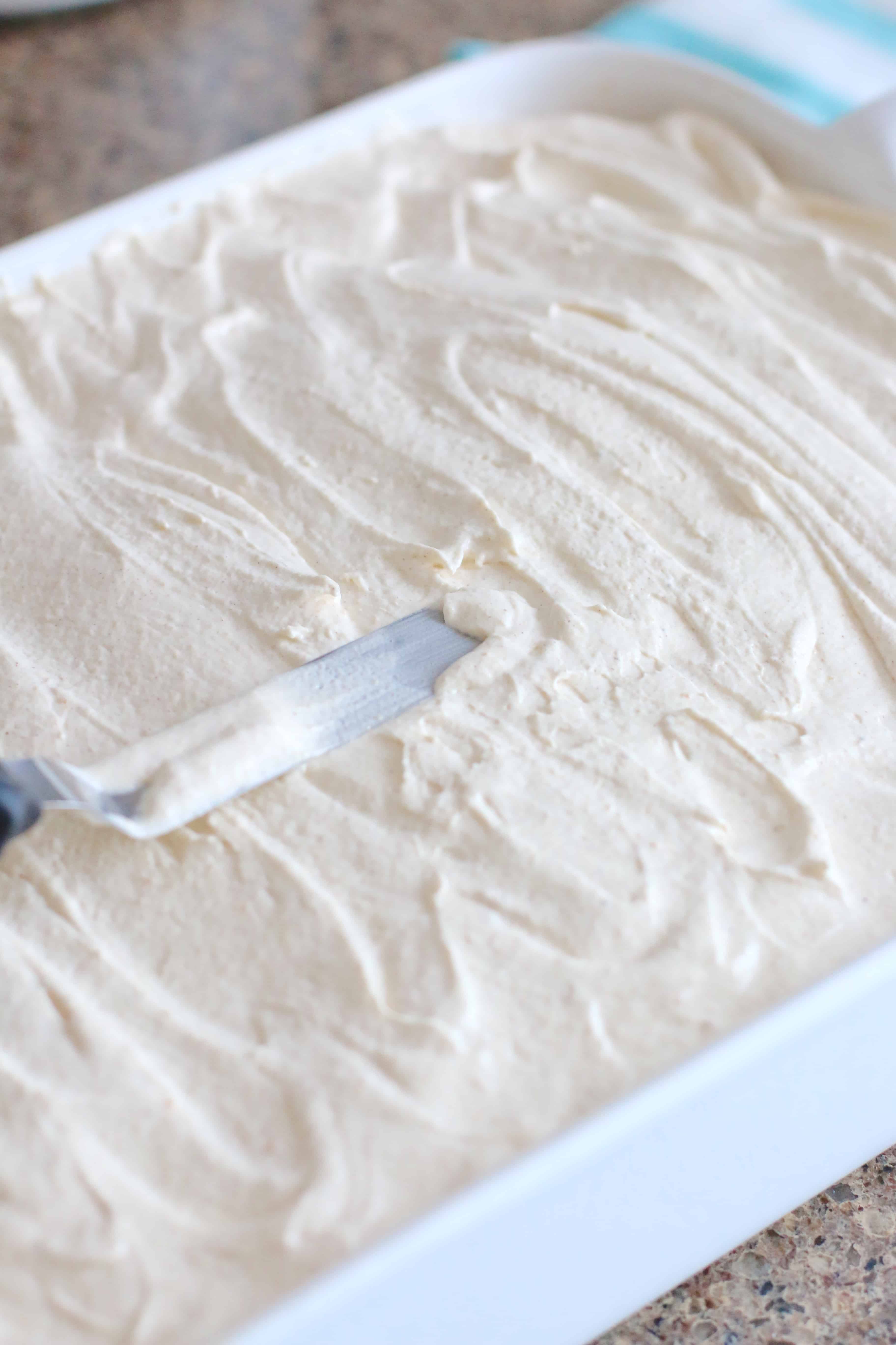 pumpkin spice whipped topping being spread with a spatula onto the cooled cake.