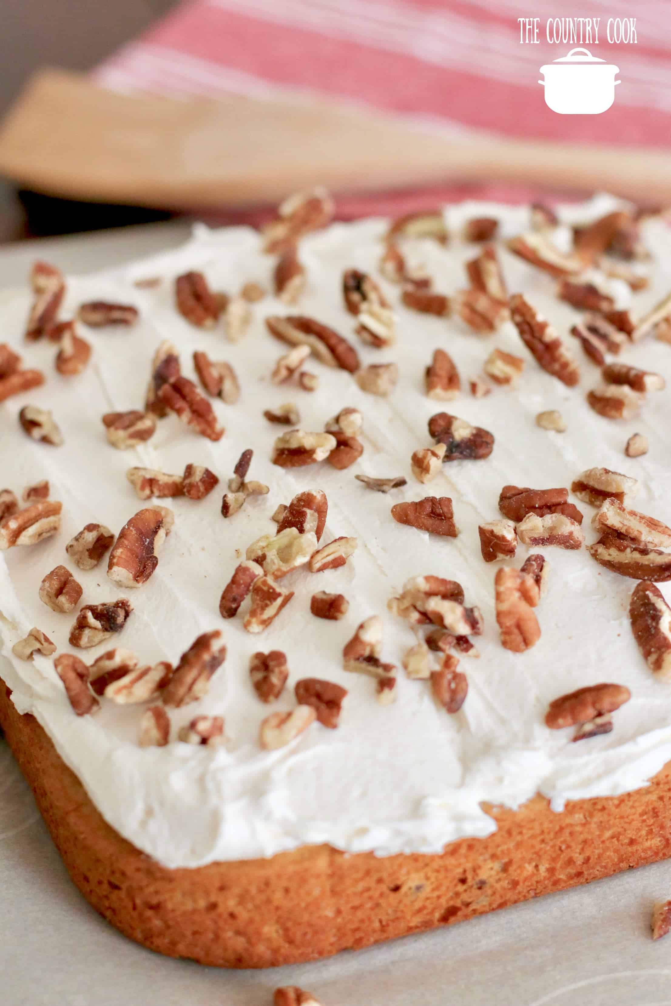 Sweet Potato Cake with Fluff Frosting and chopped pecans shown on parchment paper. 