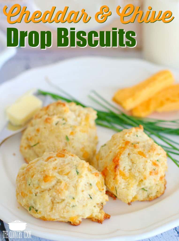 Cheddar and Chive Drop Biscuits recipe from The Country Cook. Three biscuits shown n a white plate with cheese and chives in the background.