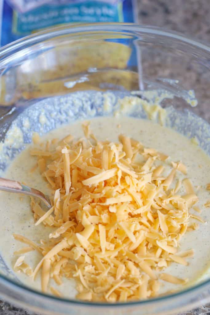 shredded sharp cheddar cheese added to Mexican cornbread batter in a large bowl