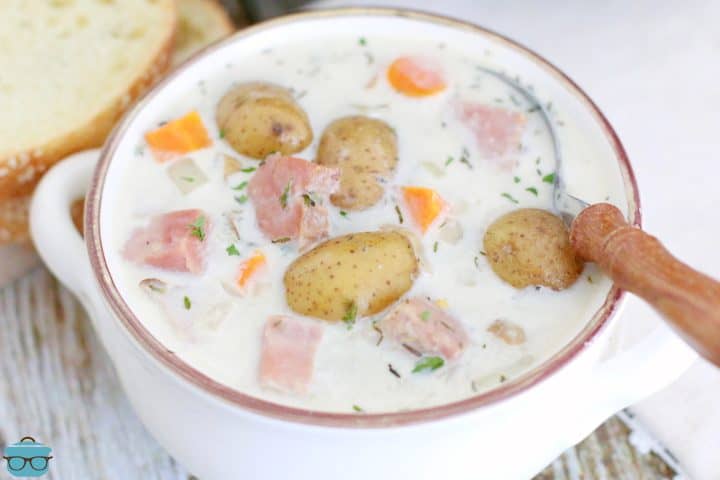 closeup photo of creamy ham and potato soup in a white bowl with a spoon.
