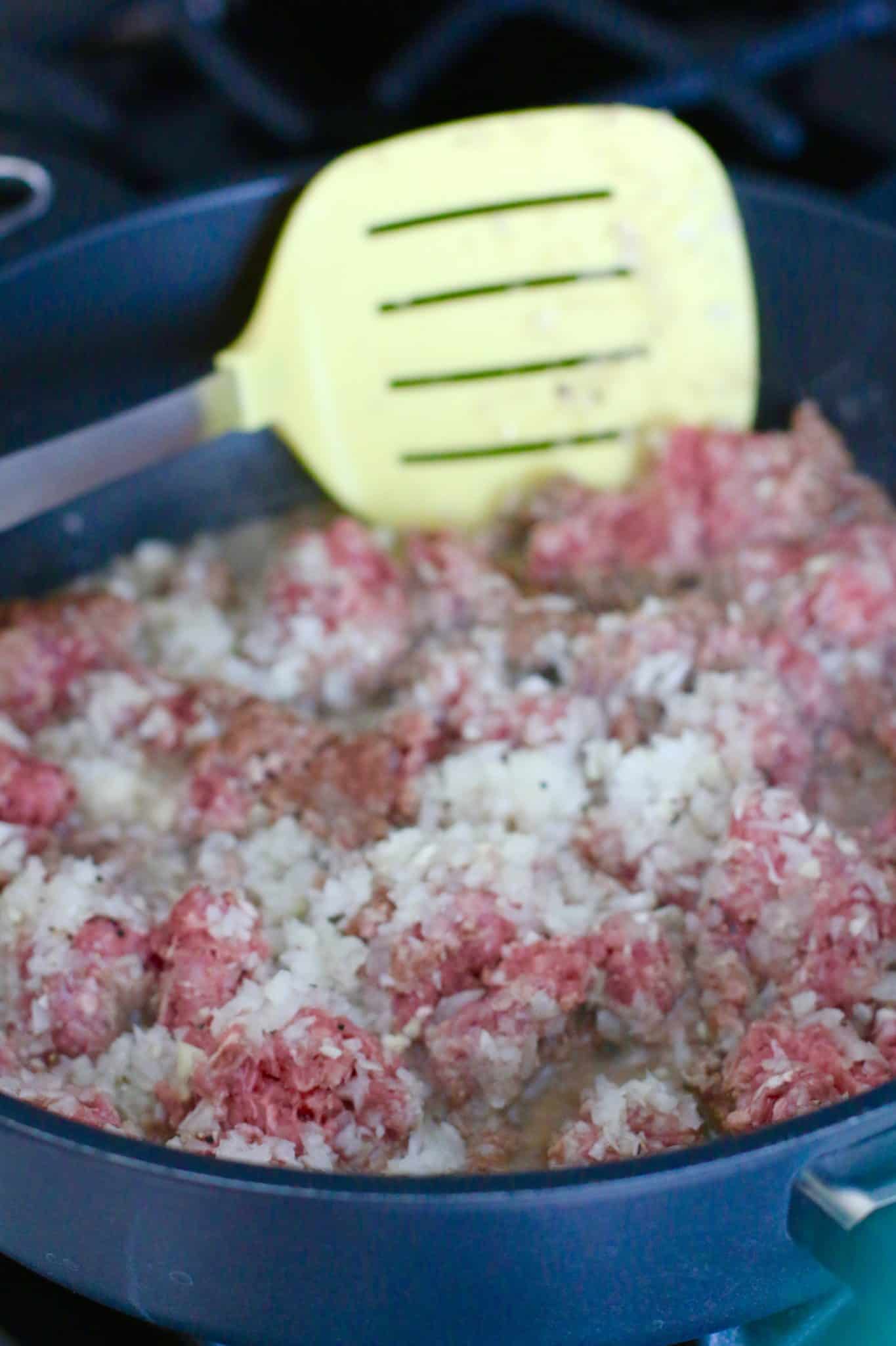 ground beef and diced onions cooking in a large skillet. 