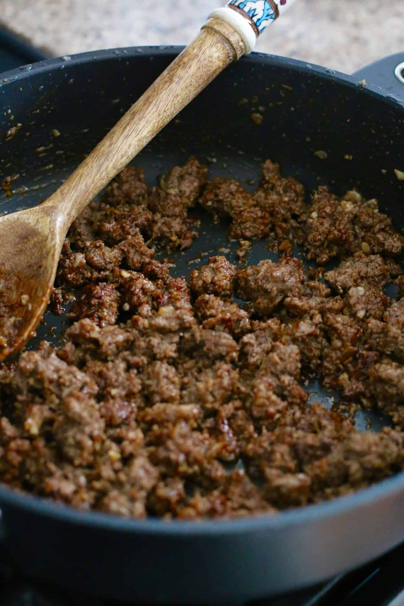 fully cooked taco ground beef with a wooden spoon in a black skillet.