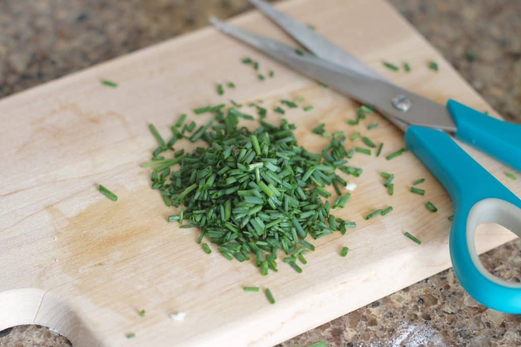 chopped chives in a wooden board and scissors to the side.