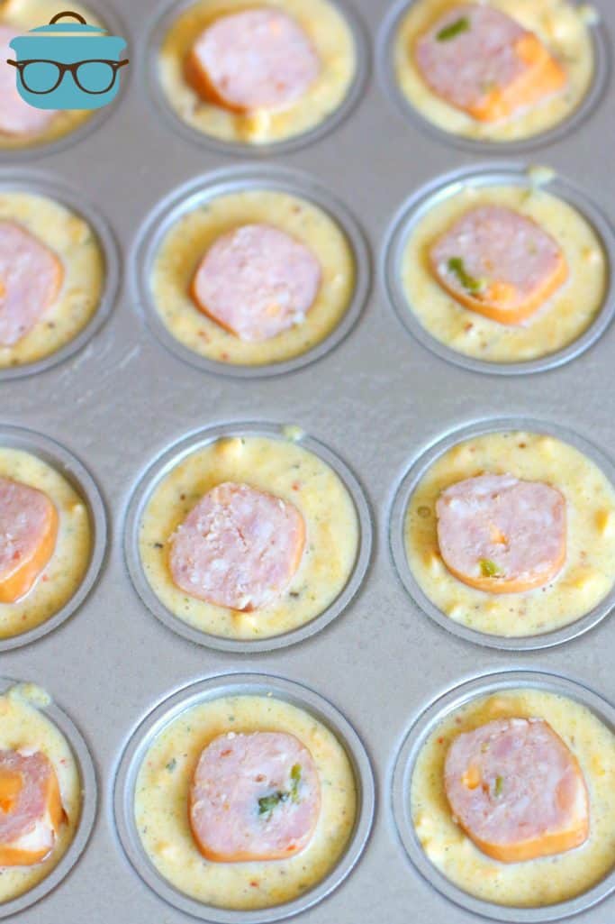 Mexican cornbread batter topped with sliced sausage in a muffin tin