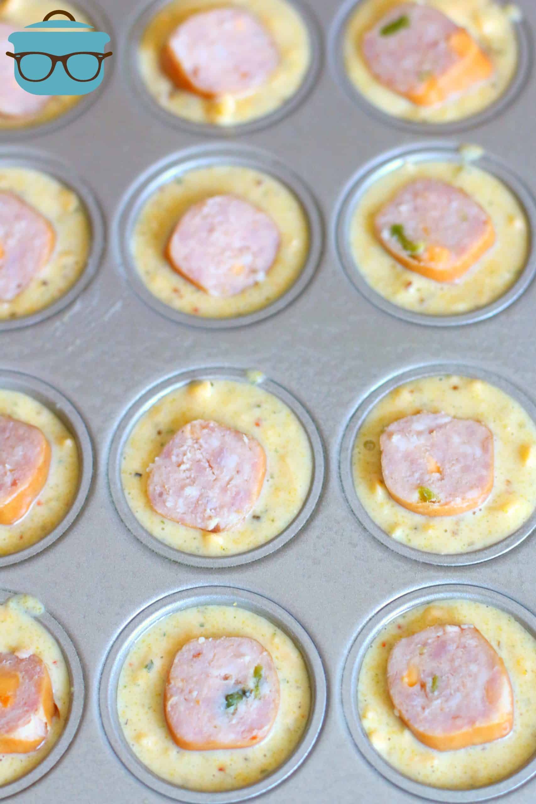 Mexican cornbread batter topped with sliced sausage in a muffin tin.